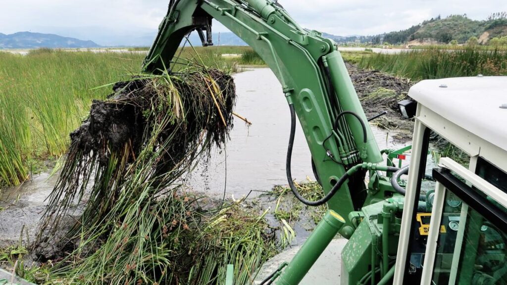 Watermaster dredger removing invasive vegetation from a lake by raking