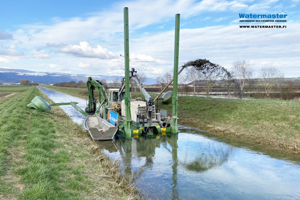 Watermaster dredging a narrow river in Switzerland. Maintaining irrigation channels to secure reliable water supply for local agriculture in Switzerland.